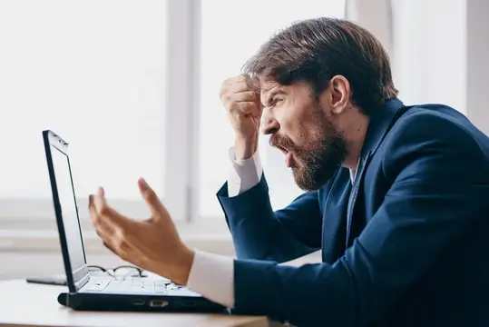 Уставший бородатый мужчина в костюме эмоционально реагирует на ноутбук