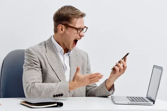 Мужчина в очках кричит на смартфон за рабочим столом