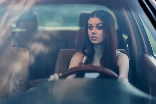 Молодая темноволосая девушка за рулём автомобиля смотрит вперёд