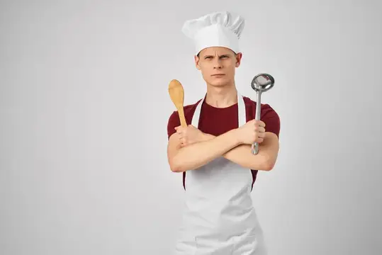 Повар-мужчина в белом фартуке, кухонная утварь, приготовление изысканной еды