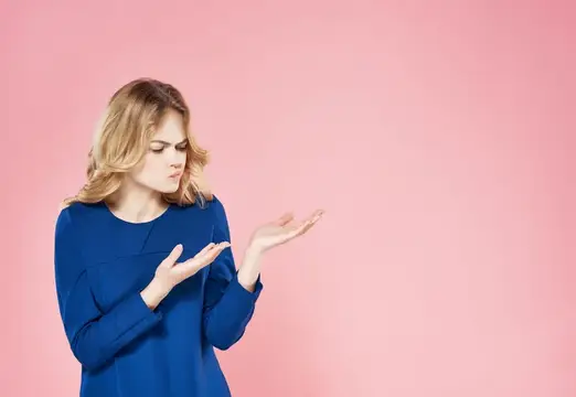 Блондинка в синем платье недовольно смотрит на протянутые ладони на розовом фоне