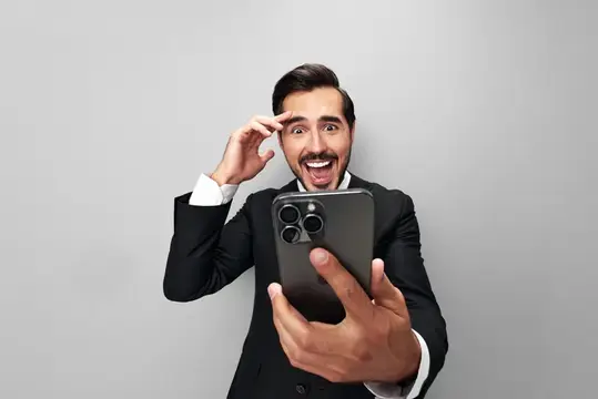 Удивлённый мужчина в костюме смотрит в смартфон и жестикулирует