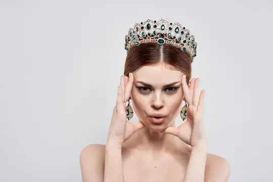 Молодая женщина в короне с изумрудами дует на ладони