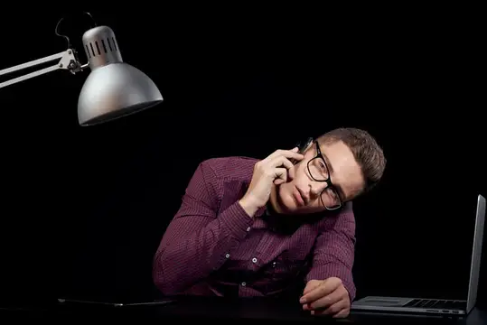 Уставший мужчина в очках говорит по телефону за рабочим столом