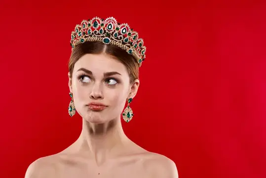 Молодая женщина в роскошной короне с драгоценными камнями на красном фоне