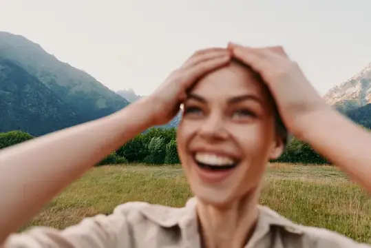 Смеющаяся девушка держится за голову на фоне гор