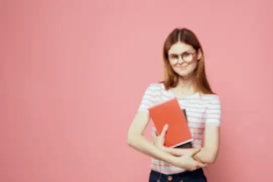 Улыбчивая девушка в очках с красной книгой на розовом фоне