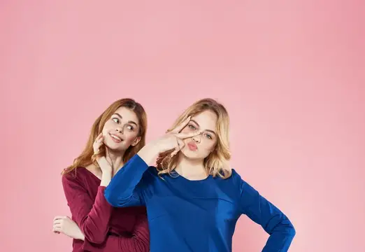 Две молодые женщины в синем и бордовом позируют на розовом фоне