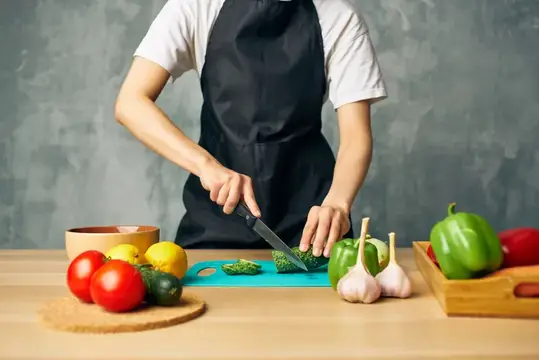Повар в чёрном фартуке нарезает брокколи на кухне