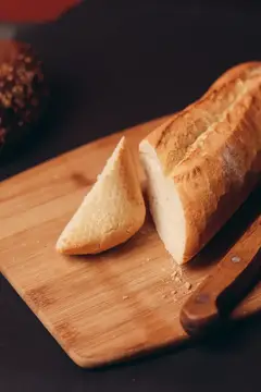 Нарезанный багет лежит на деревянной доске рядом с ножом