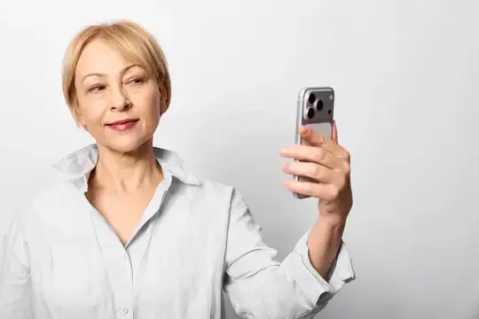 Светловолосая женщина делает селфи на смартфон на светлом фоне