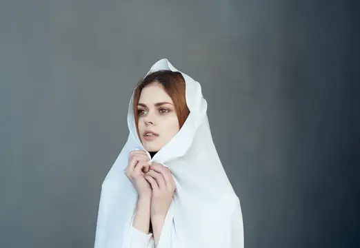 Рыжеволосая девушка в белом капюшоне на сером фоне