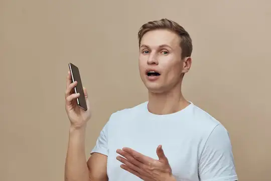 Удивлённый парень с телефоном в руке на бежевом фоне