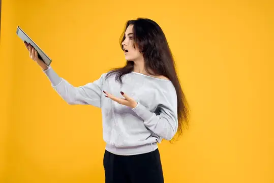 Удивлённая темноволосая девушка с планшетом на жёлтом фоне