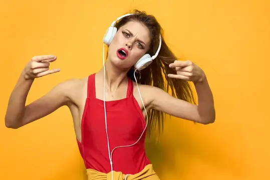 Женщина в наушниках слушает музыку, красная футболка, эмоции, мода, образ жизни на желтом фоне