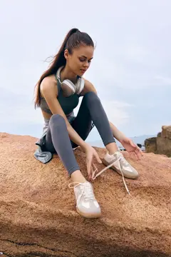 Спортивная девушка с наушниками завязывает шнурки на скале