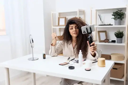 Брюнетка записывает видео о косметике на смартфон за белым столом