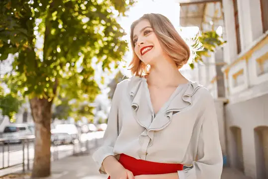 Улыбающаяся светловолосая женщина в блузке на солнечной улице