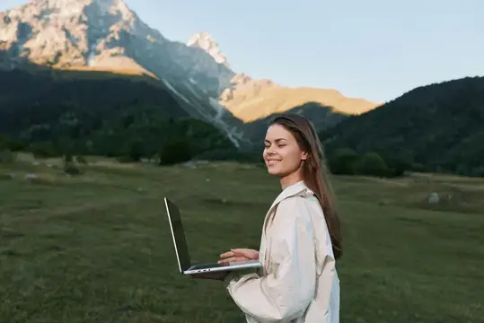 Улыбающаяся девушка с ноутбуком на фоне гор