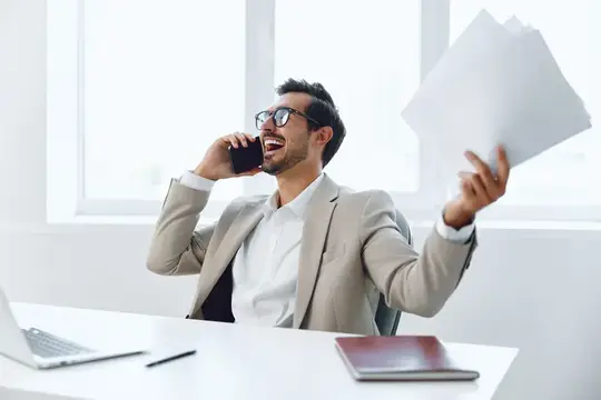 Улыбающийся бородатый мужчина в офисе говорит по телефону с бумагами