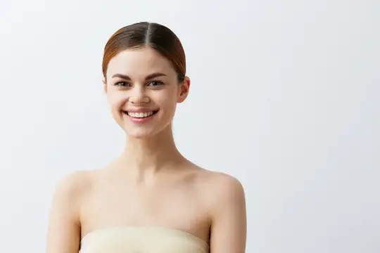 Улыбающаяся темноволосая девушка с открытыми плечами на светлом фоне