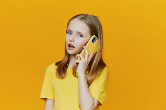 Светловолосая девочка в жёлтой футболке удивлённо слушает телефон