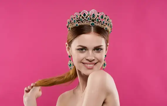 Улыбающаяся девушка в короне с изумрудами на розовом фоне