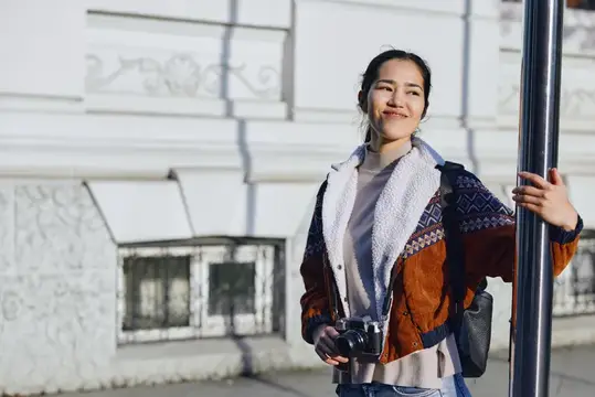 Улыбающаяся азиатская девушка с фотокамерой у светлого здания