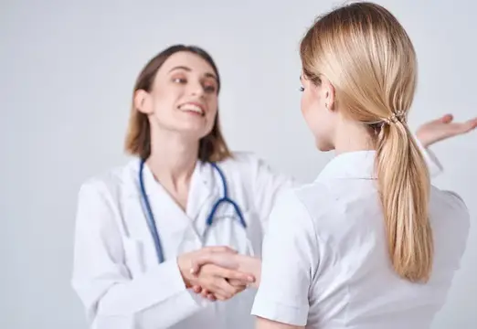 Две женщины-врача в белых халатах пожимают руки на приёме