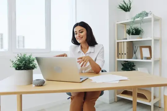 Улыбающаяся темноволосая женщина работает за ноутбуком в светлом офисе