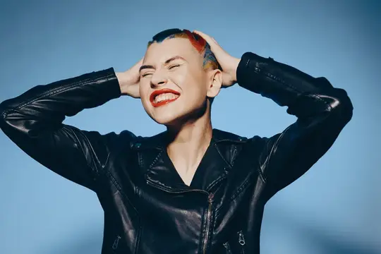 Улыбающаяся девушка с короткой цветной стрижкой в черной кожаной куртке