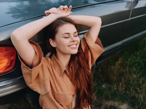 Улыбающаяся девушка с закрытыми глазами у чёрного автомобиля