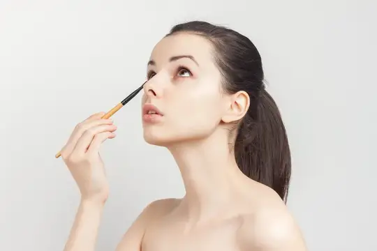 Женщина наносит маску на лицо кисточкой для макияжа