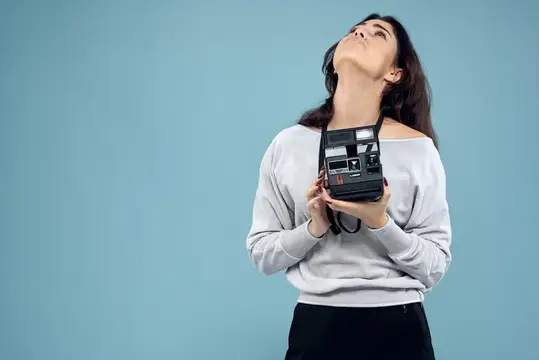 Молодая женщина с ретро-фотоаппаратом смотрит вверх на голубом фоне