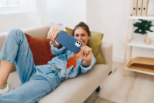 Молодая женщина лежит на диване и делает селфи на смартфон
