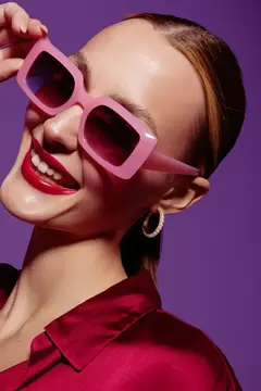 Улыбающаяся девушка в розовых солнцезащитных очках на фиолетовом фоне