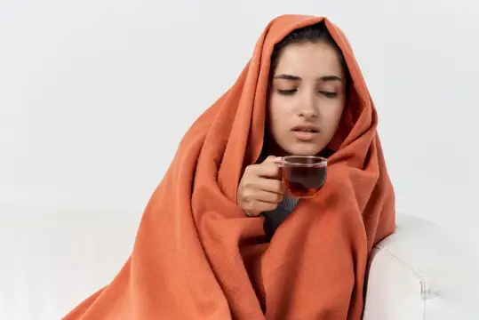 Девушка, укутанная в оранжевый плед, пьёт чай