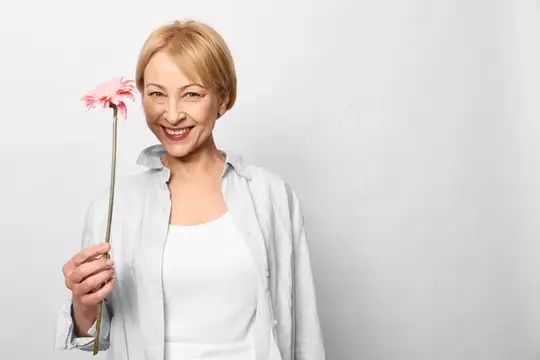 Улыбчивая блондинка держит розовую герберу на белом фоне