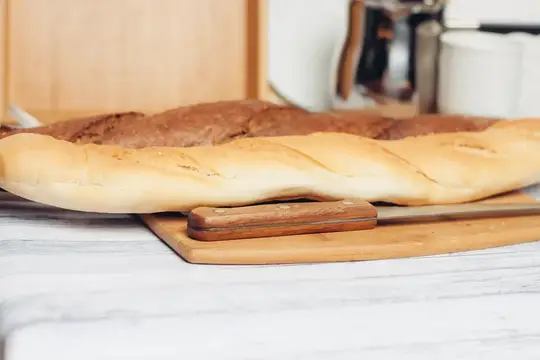 Свежеиспечённый багет с деревянной ручкой ножа на кухонном столе