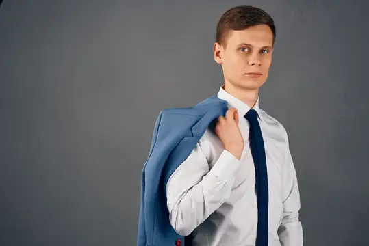 Молодой мужчина в белой рубашке с галстуком держит синий пиджак на плече