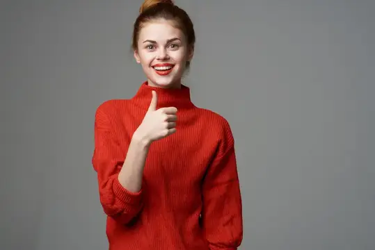 Улыбающаяся девушка в красном свитере показывает большой палец вверх