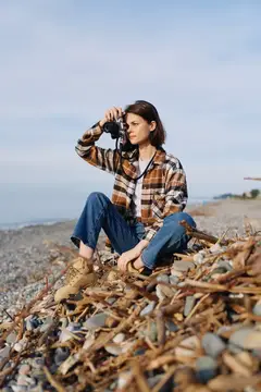 Девушка с фотокамерой сидит на камнях у моря