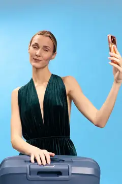Улыбающаяся женщина с чемоданом делает селфи на голубом фоне