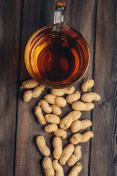 Стакан янтарного напитка и рассыпанный арахис на тёмных деревянных досках