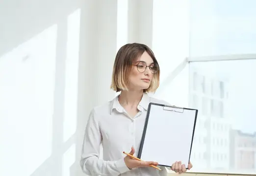 В комнате женщина занимается финансами, работая с деловыми документами у окна