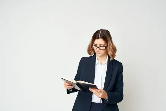Женщина в очках и деловом костюме читает книгу на светлом фоне
