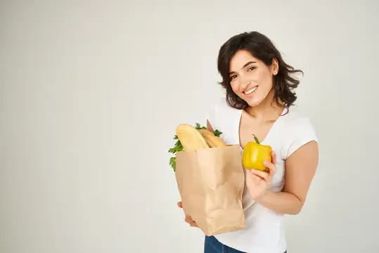 Улыбающаяся брюнетка с бумажным пакетом продуктов и жёлтым перцем