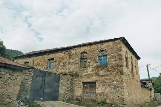 Старый каменный дом с арочными окнами под облачным небом