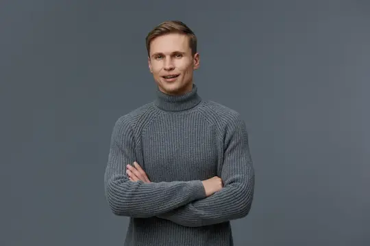Улыбающийся мужчина в серой водолазке скрестил руки на груди
