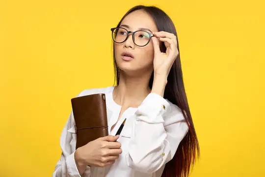 Азиатская девушка в очках с блокнотом на жёлтом фоне